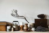 Decorative shelf with various items including a branch, candles, and wooden boxes against a plain wall.