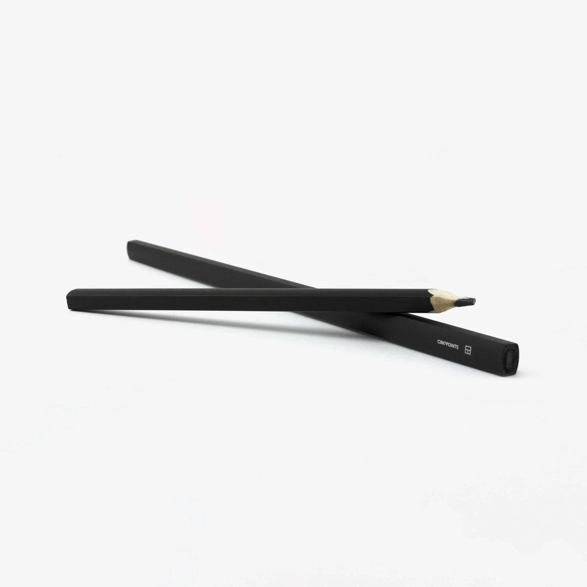 Two black graphite pencils crossed over each other on a clean white background, with one pencil showing its sharpened graphite tip.