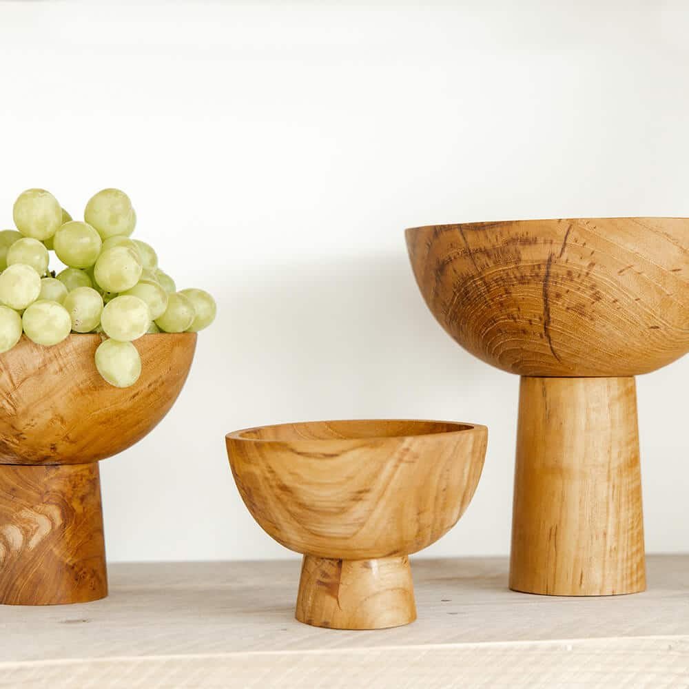 Three wooden bowls of varying sizes with a cluster of grapes on a light background