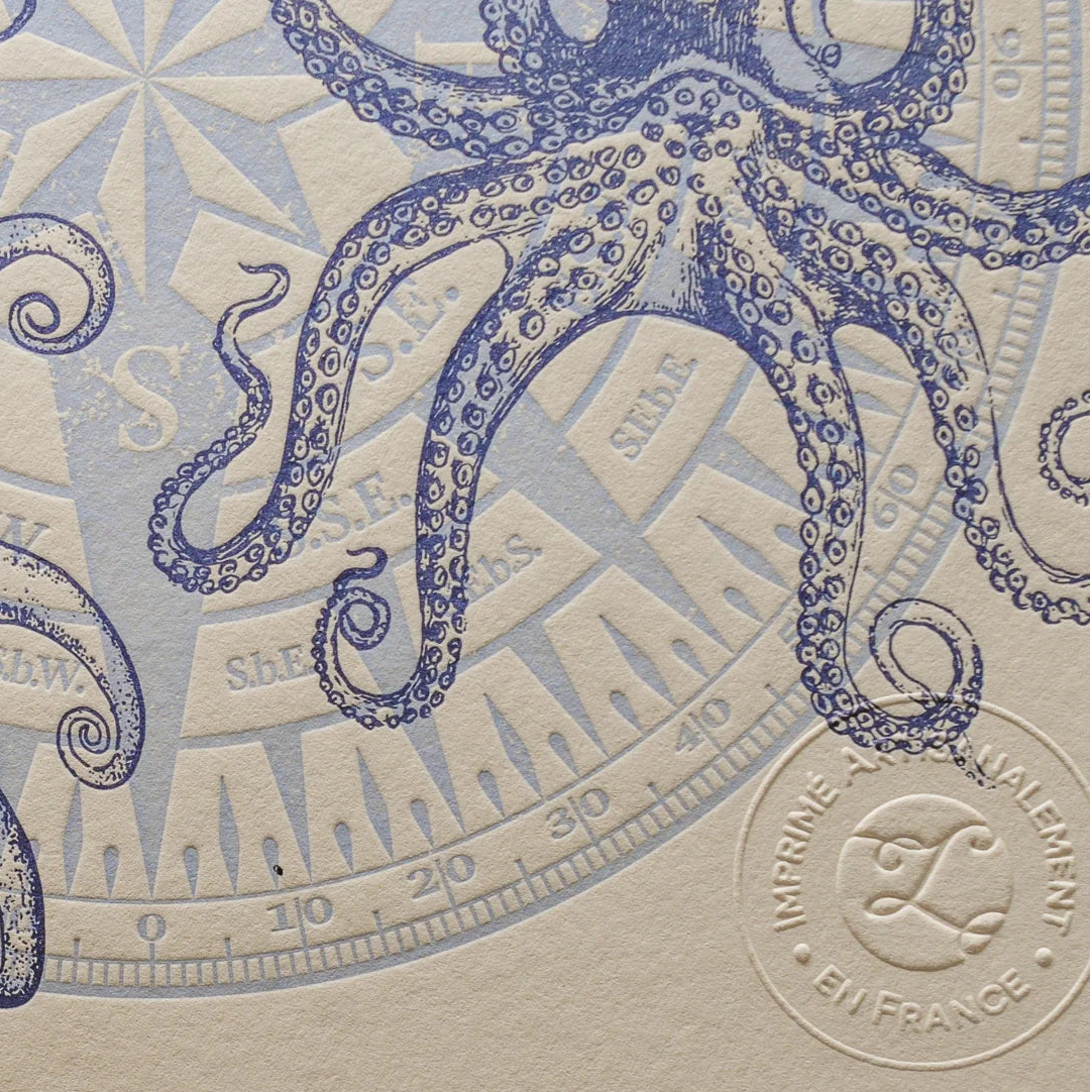 A close up of vintage-style illustrated art print with illustrations of an octopus and compass in the background on off-white cotton paper, showing the embossed stamp of authenticity.
