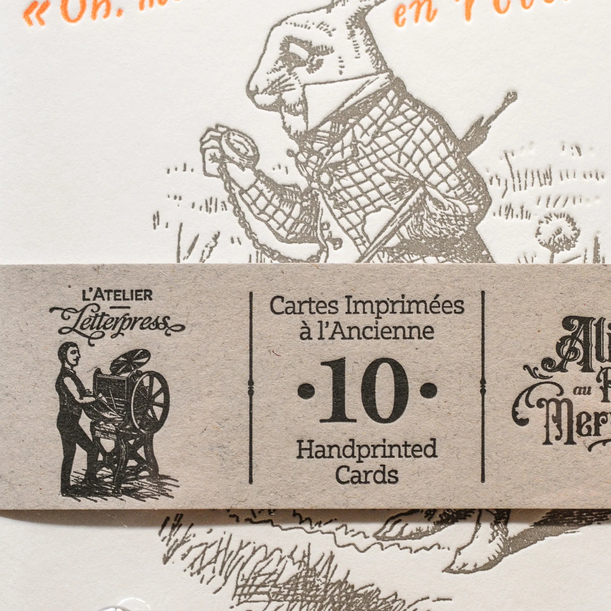 A close up of a art print card of Alice in Wonderland, with a recycled brown paper strip across the card.