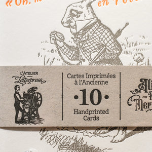 A close up of a art print card of Alice in Wonderland, with a recycled brown paper strip across the card.