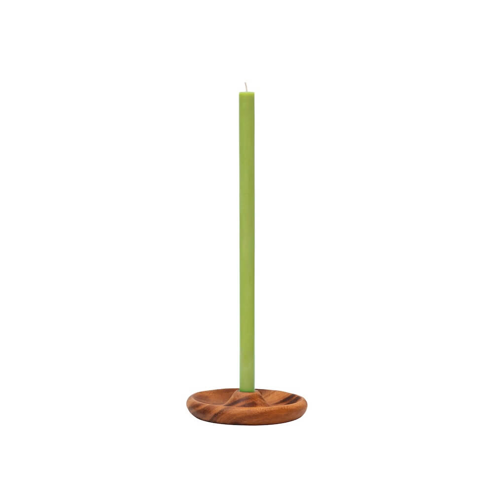 A tall, slim light green candle standing upright in a round wooden candle holder with a natural brown wood grain finish, set against a plain white background.