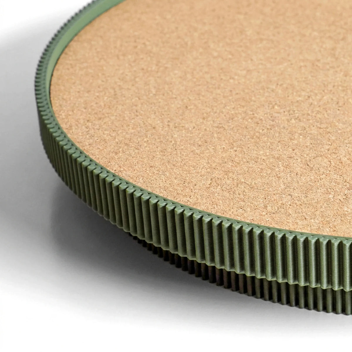 Close-up of a dark green circular serving tray with a cork top on a light gray background