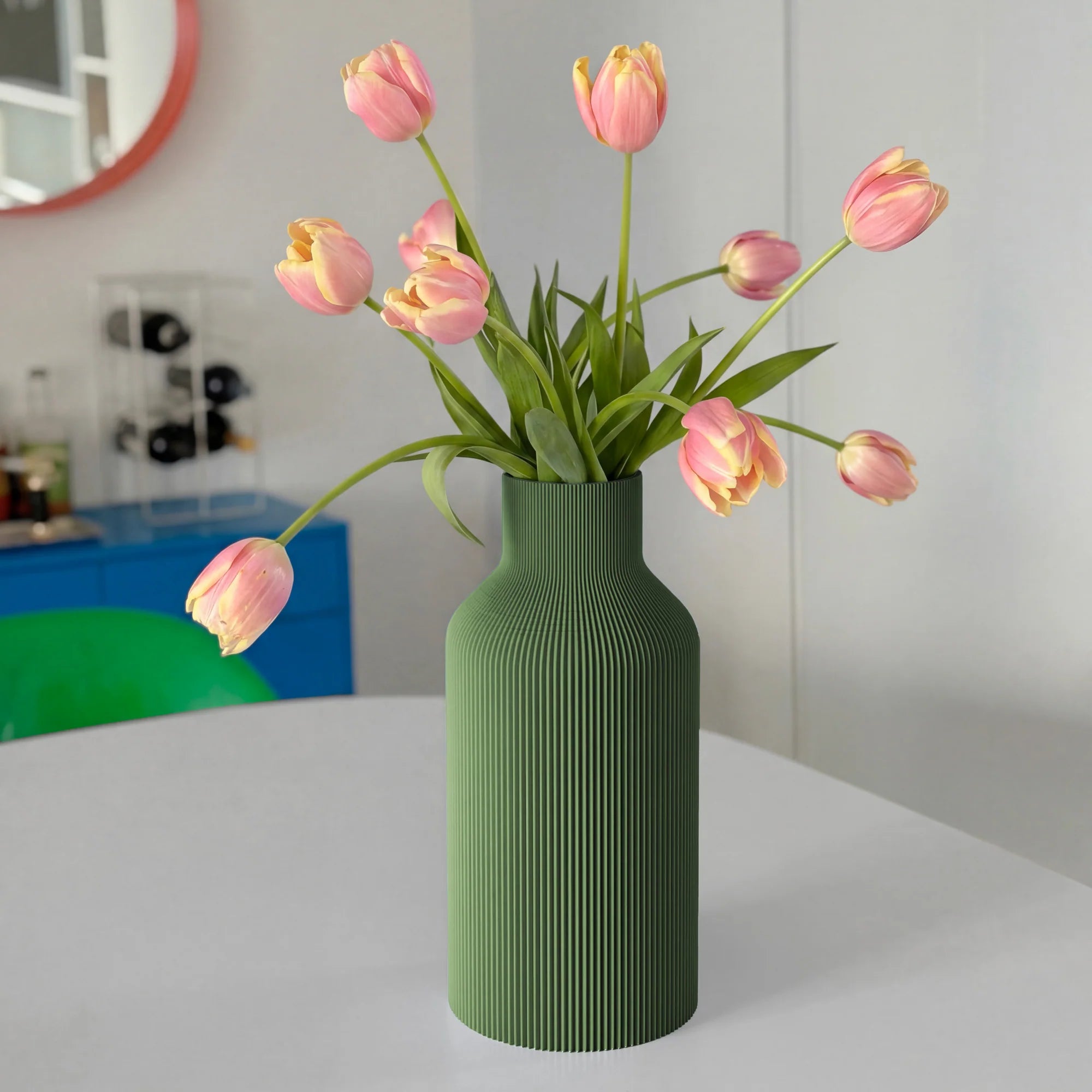 Olive green ribbed vase with pink tulips on a white table