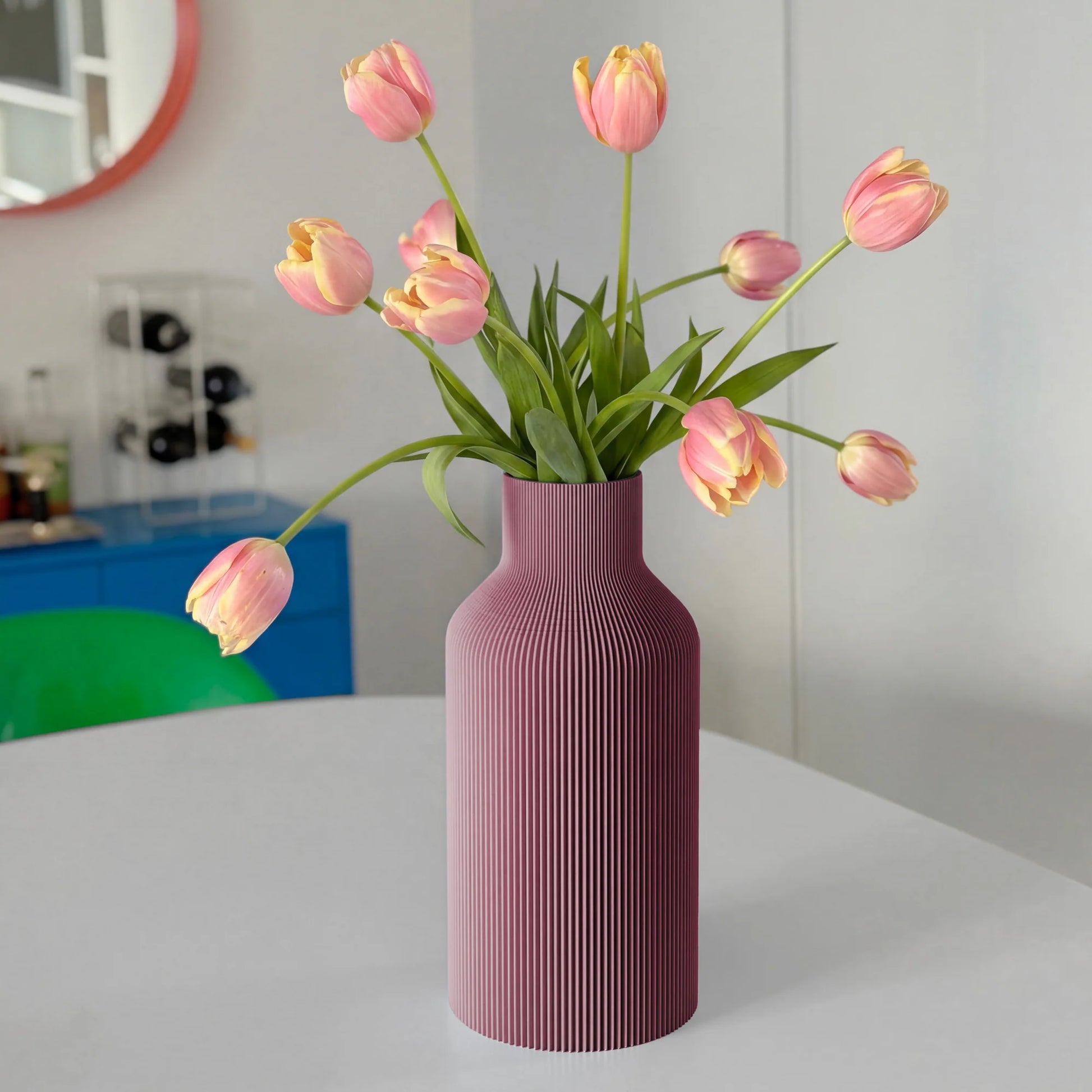 Purple ribbed vase with pink tulips on a white table.