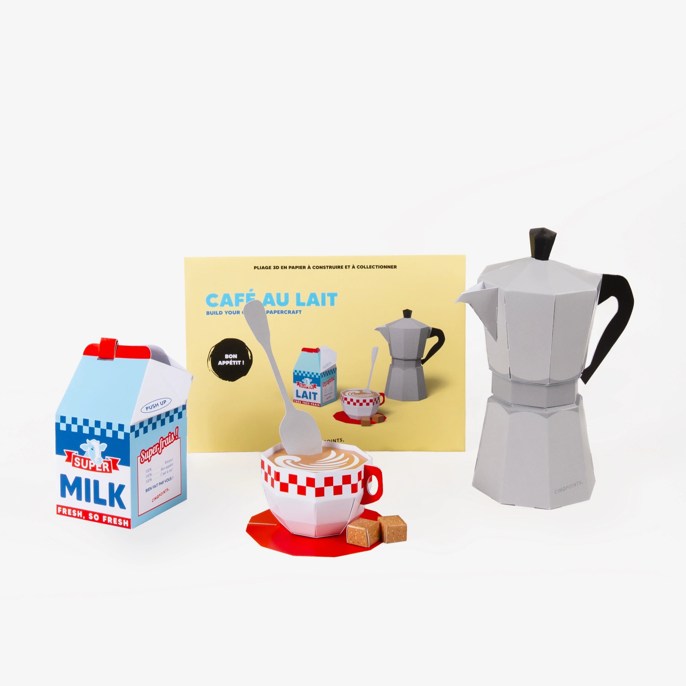 A light yellow cardboard envelope for a cafe scene paper model set behind, and in front 3D paper models featuring illustrations of a gray moka pot, a milk carton, and a red-and-white checkered coffee cup, photographed on a clean white background.