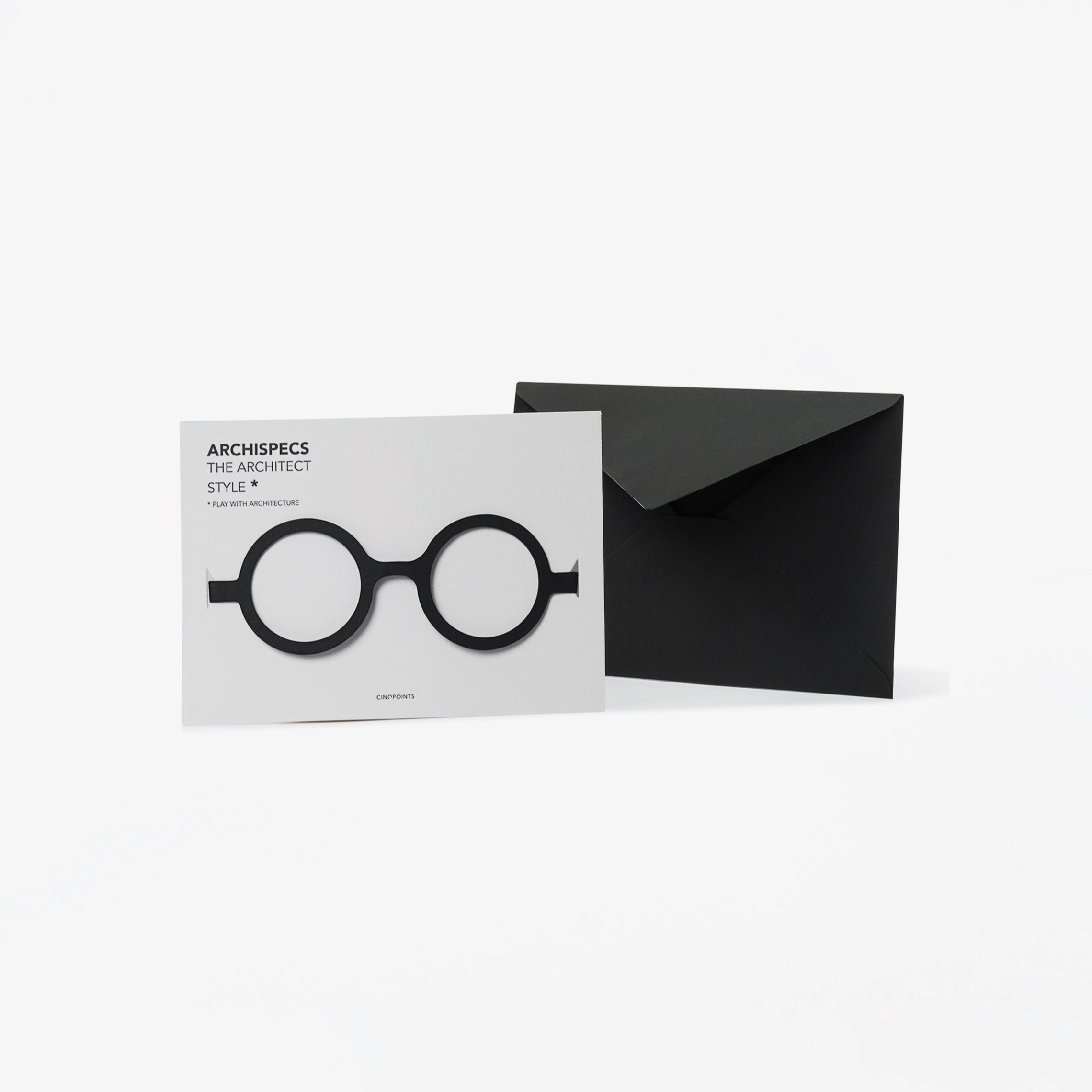 A minimalist architectural card set featuring a white card with black cut out cardboard circular eyeglass, shown next to a black envelope on a light gray background.