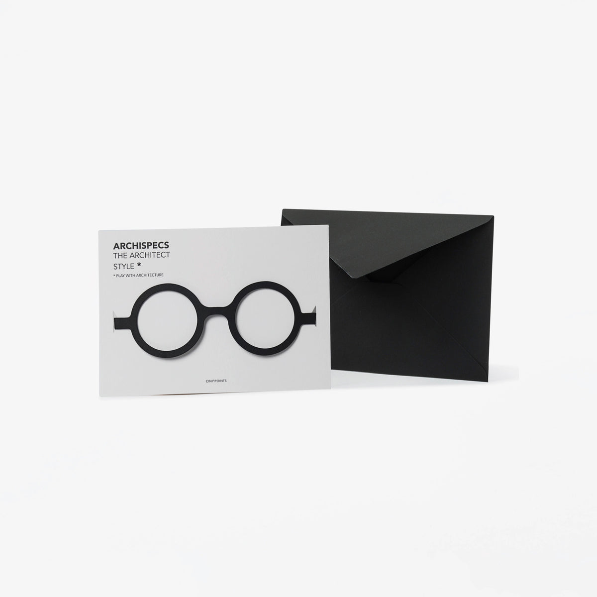 A minimalist architectural card set featuring a white card with black cut out cardboard circular eyeglass, shown next to a black envelope on a light gray background.