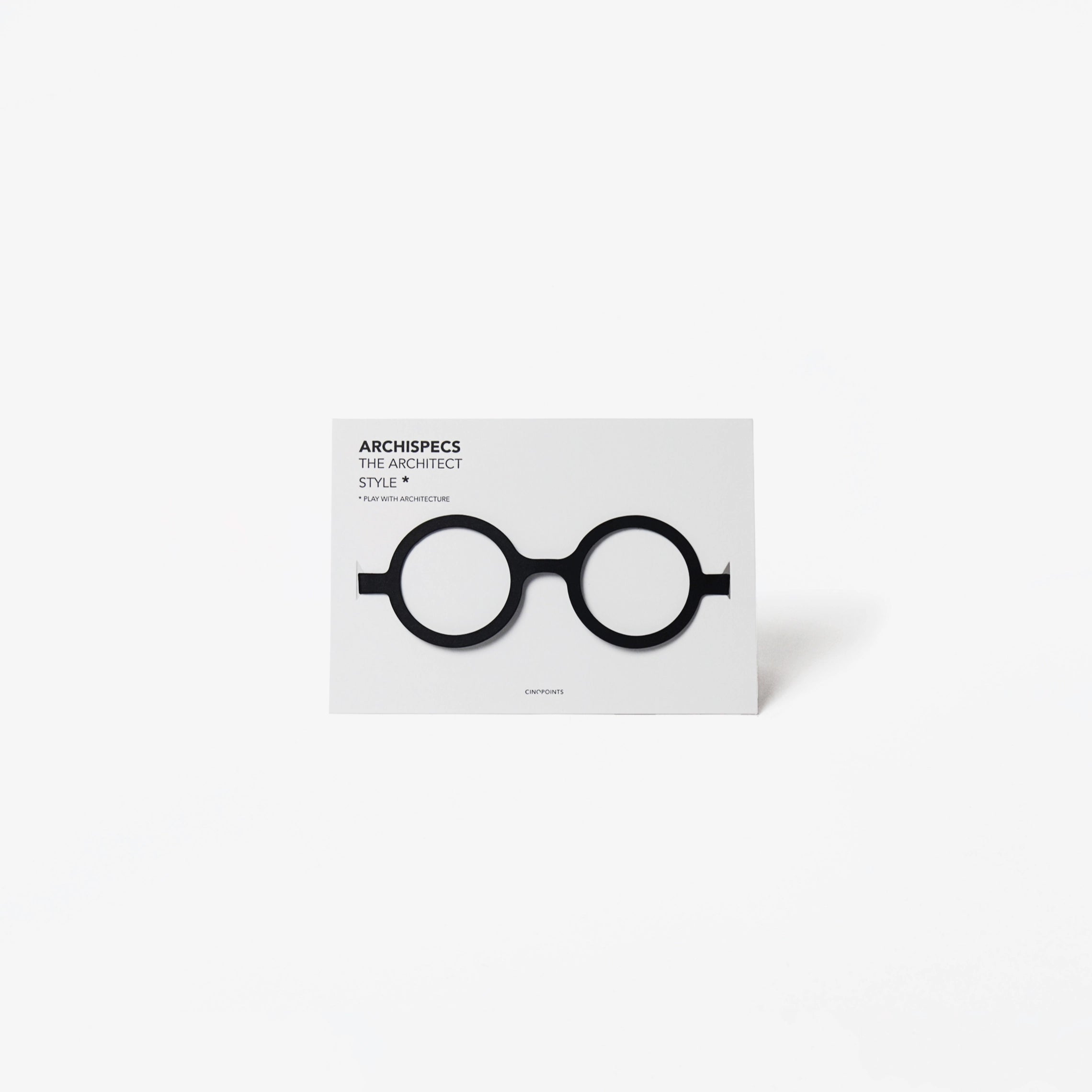 A minimalist architectural card featuring a white card with black cut out cardboard circular eyeglass, shown on a light gray background.