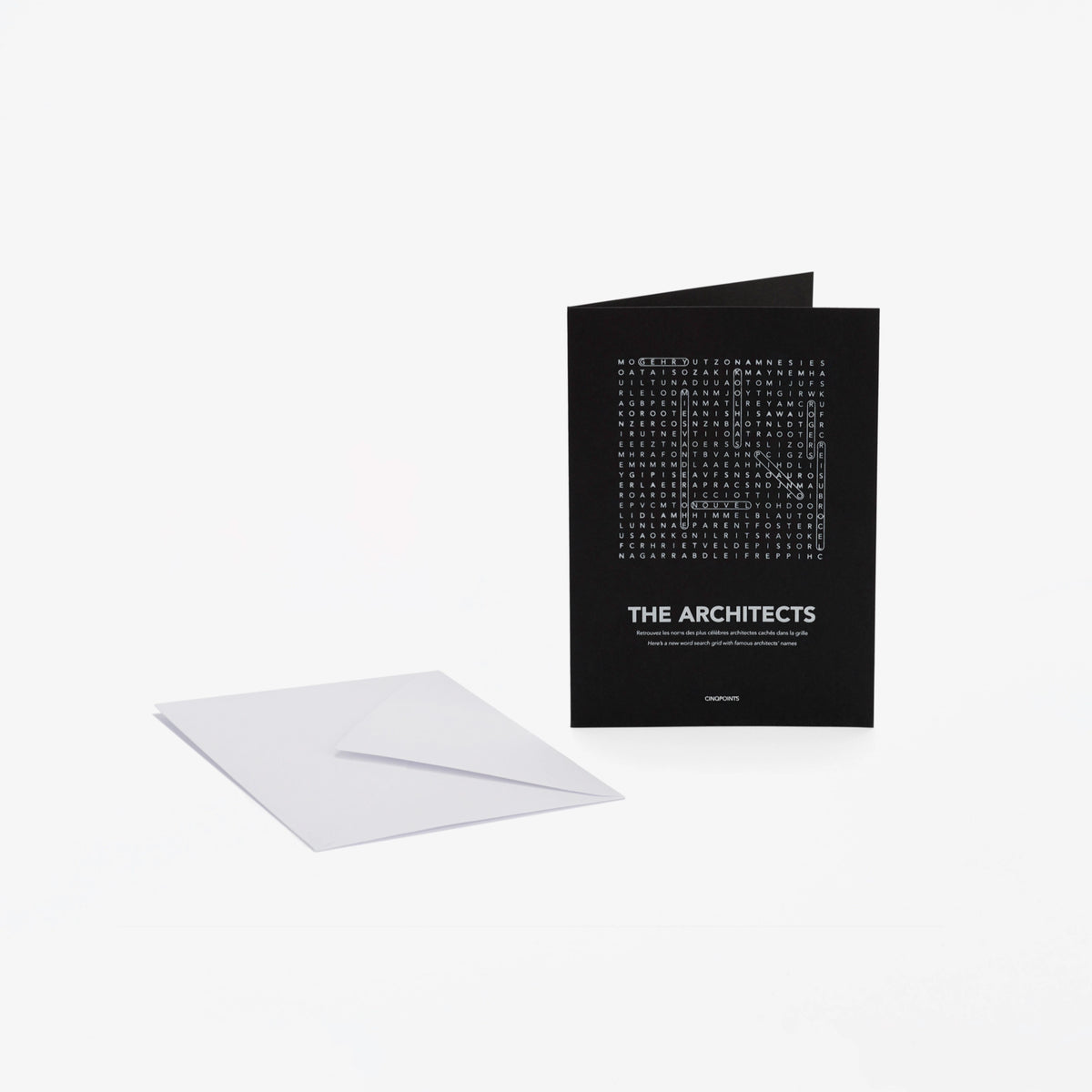 A black greeting card with white text "The Architects" and a word-search style crossword, shown standing upright next to a white envelope on a light gray background.