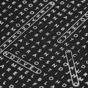 Close-up of black textured paper with dense white printed letters and several outlined word shapes, like that from a word-search style crossword.
