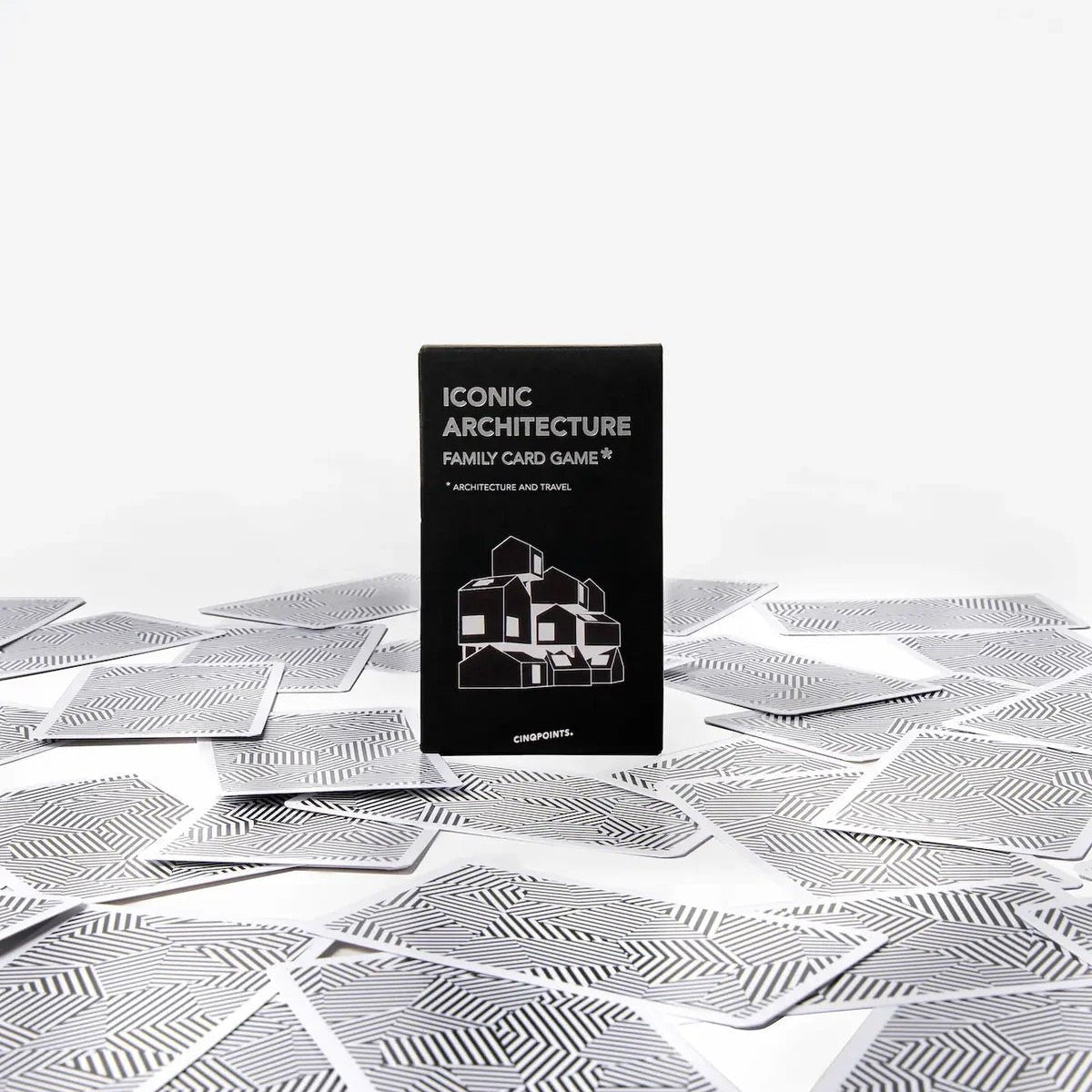 A black card game box labeled 'ICONIC ARCHITECTURE' stands upright on a white surface scattered with silver patterned cards against a clean white background.