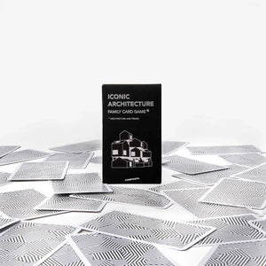 A black card game box labeled 'ICONIC ARCHITECTURE' stands upright on a white surface scattered with silver patterned cards against a clean white background.