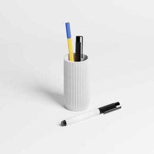 A ribbed white pen holder cup containing three pens, with a matching white pen with a black clip lying in the foreground on a clean white surface.