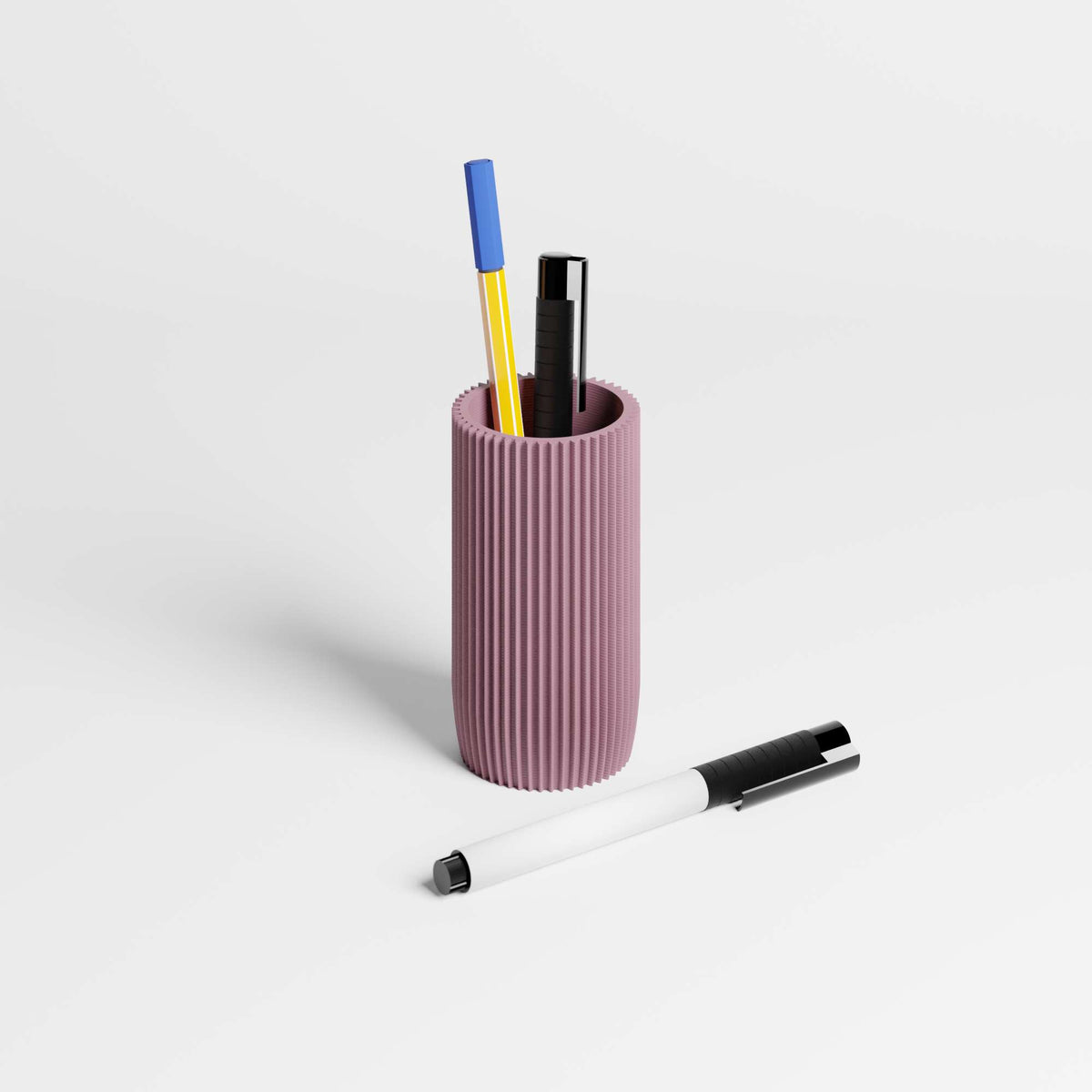 A ribbed, dusty purple cylindrical pen holder containing two pens, with a white and black pen lying in the foreground on a clean white studio background.