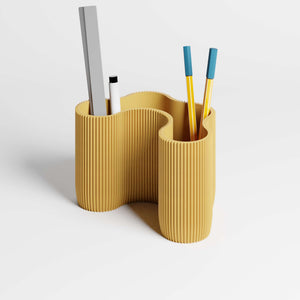 A mustard yellow ribbed desktop organiser  with a wavy, organic shape, with pens and a ruler inside it, shown on a clean white background.