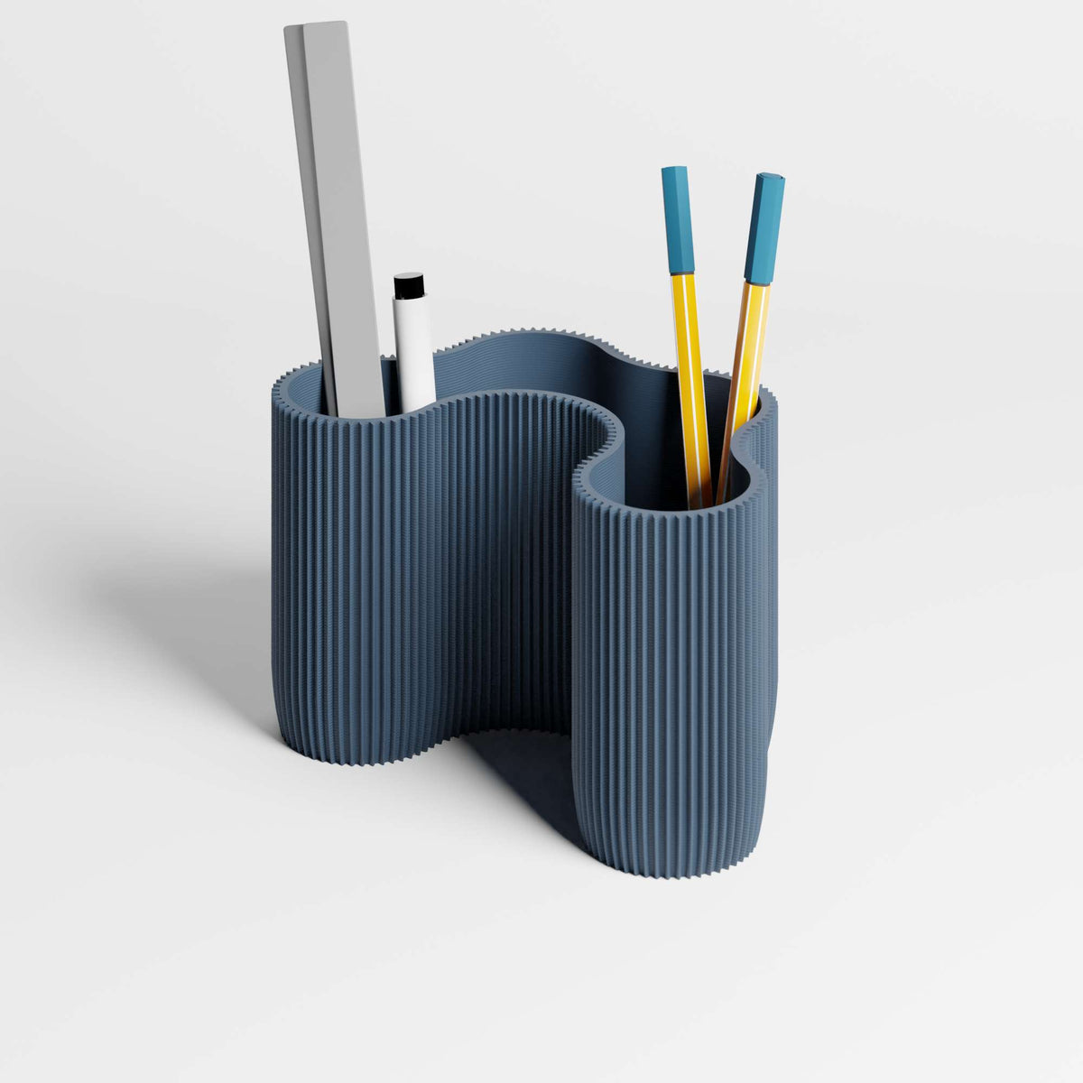A modern, sculptural ribbed desk organiser in a muted navy blue colour, shown with pens and a ruler inside on a clean light gray studio background.
