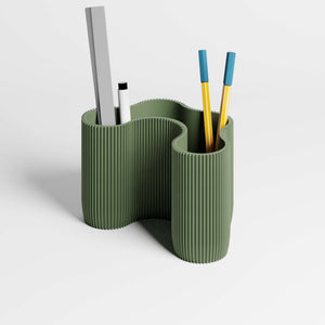 A sculptural ribbed desk organiser in a muted olive green colour, with pens and a ruler in it, shown on a clean light gray studio background.