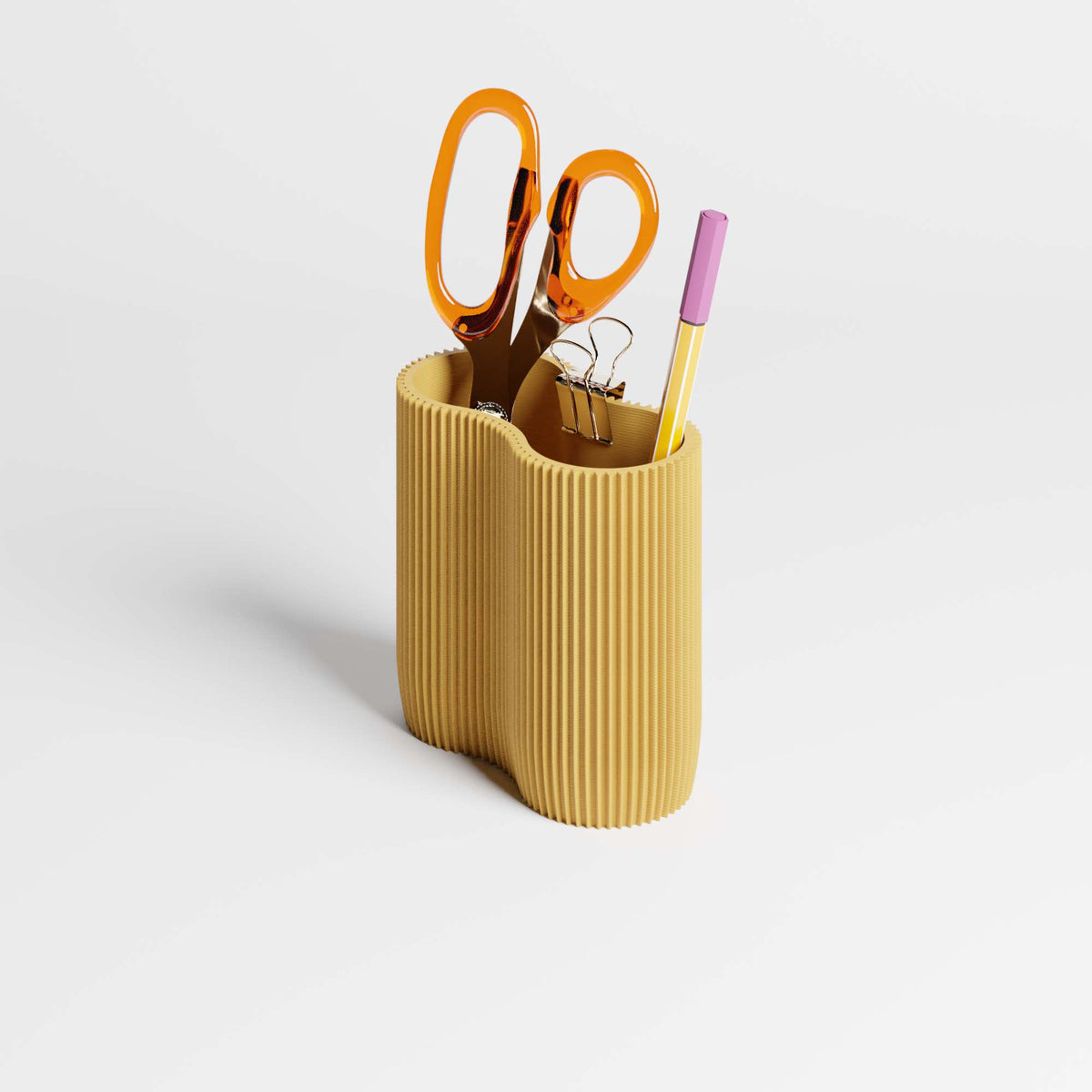 A ribbed mustard yellow pen holder or desk organiser on a light gray background, containing scissors, a black binder clip, and a yellow pen.