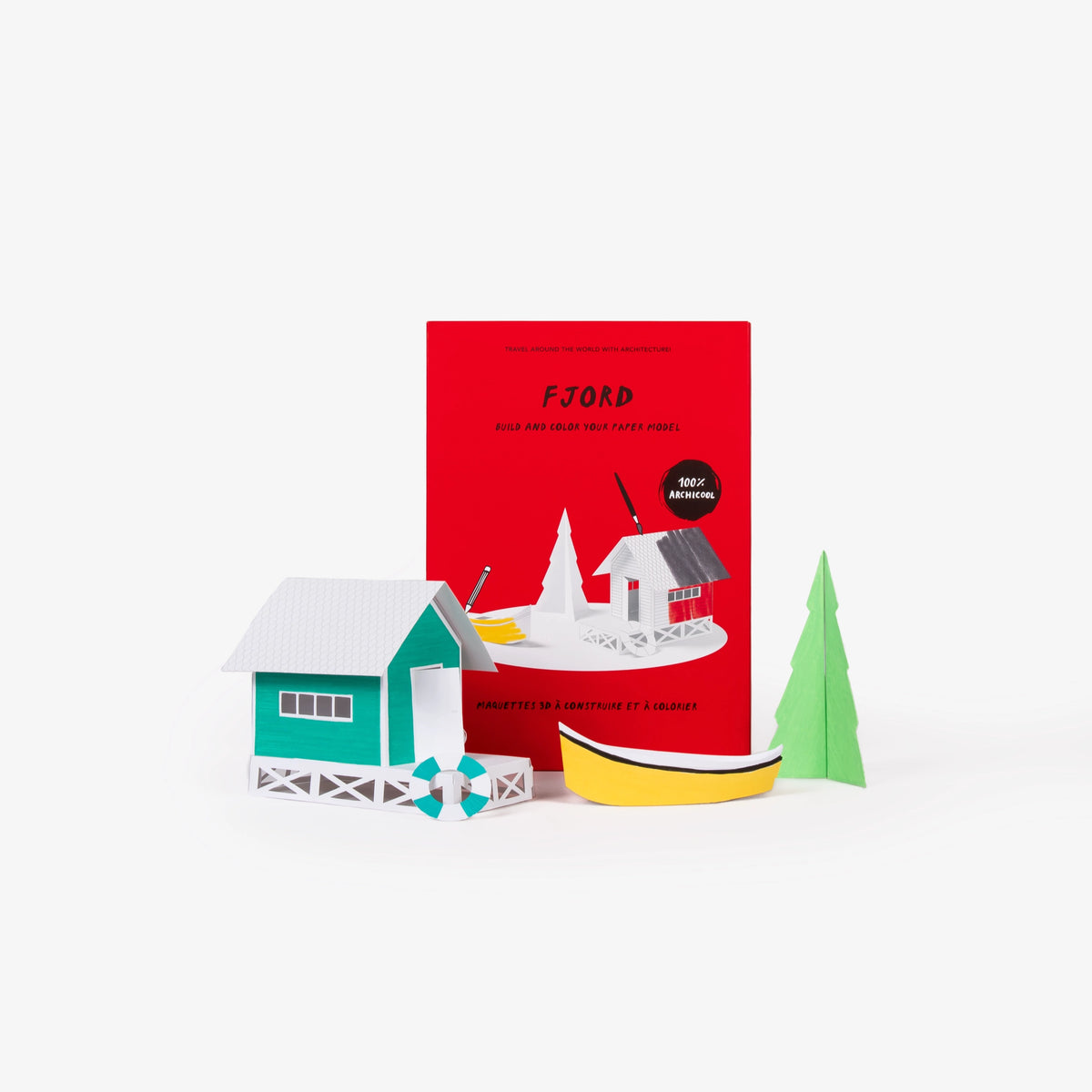 A red cardboard folder of a paper model kit stands upright behind a small 3D paper model of a green house, yellow boat, and green tree on a clean white background.