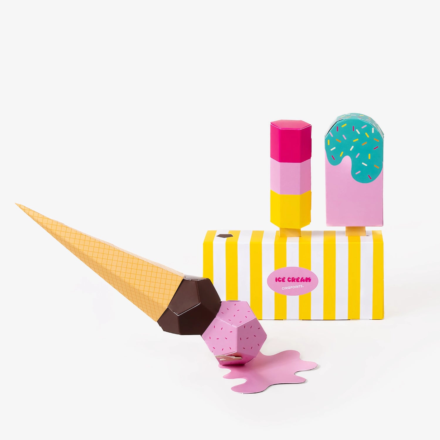 A colourful paper set of an ice cream cone on the floor partially melting, 2 different ice creams, and a striped dessert box, photographed on a clean white background.