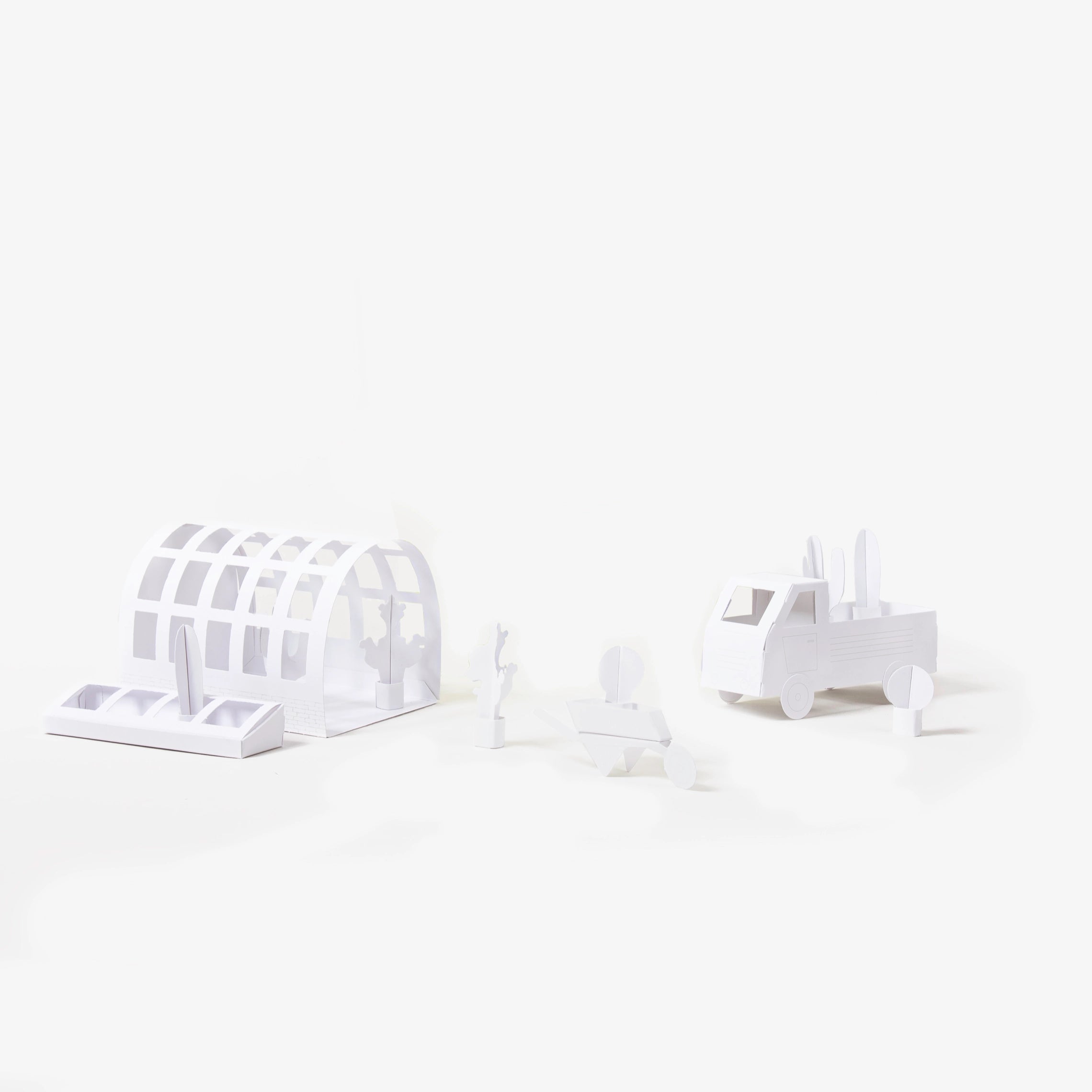 A set of minimalist white paper models, including an arched greenhouse structure, a wheelbarrow, plants and a pickup truck, arranged on a seamless white background.