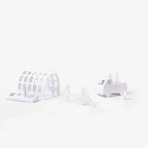 A set of minimalist white paper models, including an arched greenhouse structure, a wheelbarrow, plants and a pickup truck, arranged on a seamless white background.