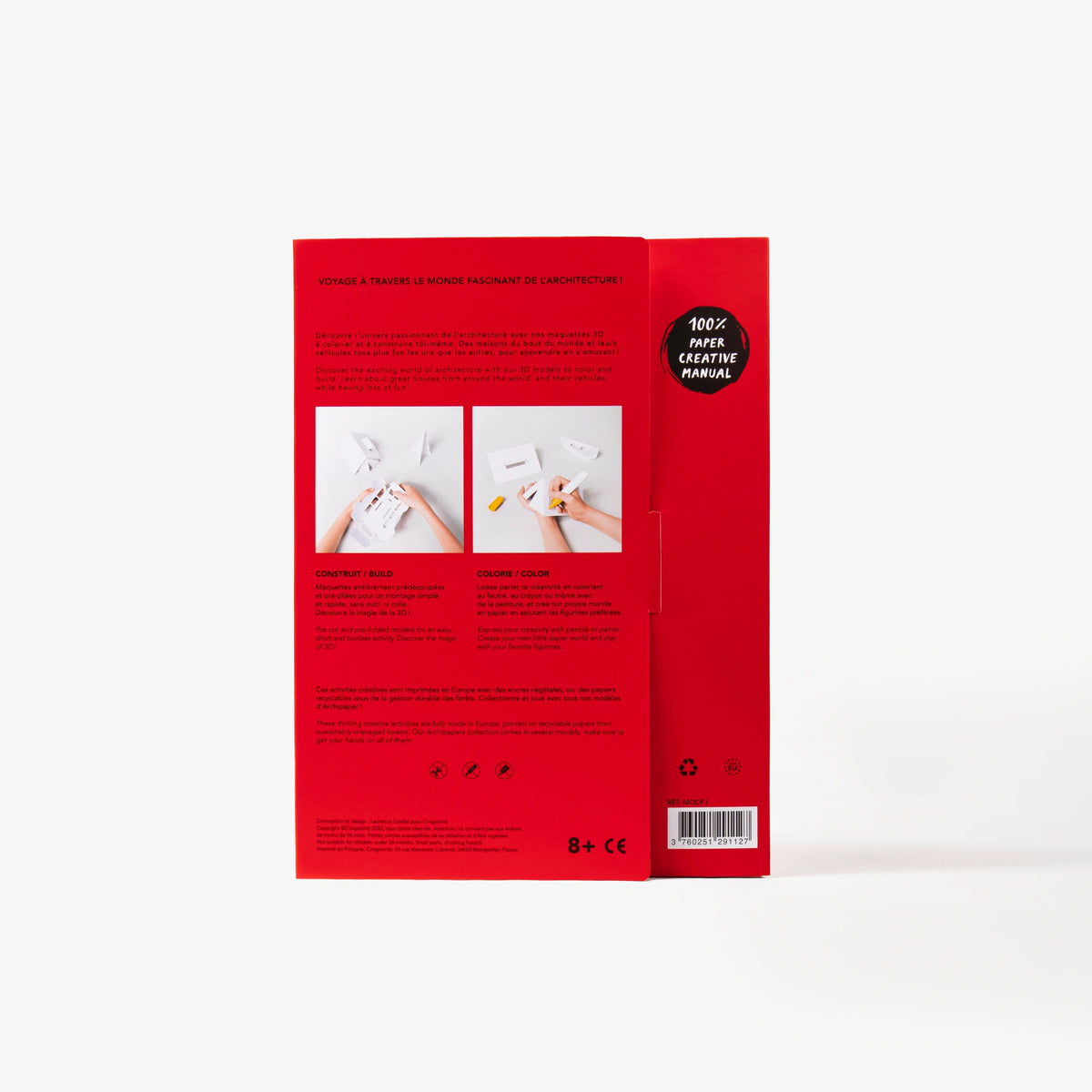 The back cover of a red cardboard folder of a paper model kit stands upright on a clean white background, showing instructional text, and two small photos of hands working with white paper.